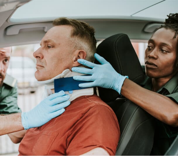 Emergency responders in blue gloves applying a cervical collar to an injured person inside a car.