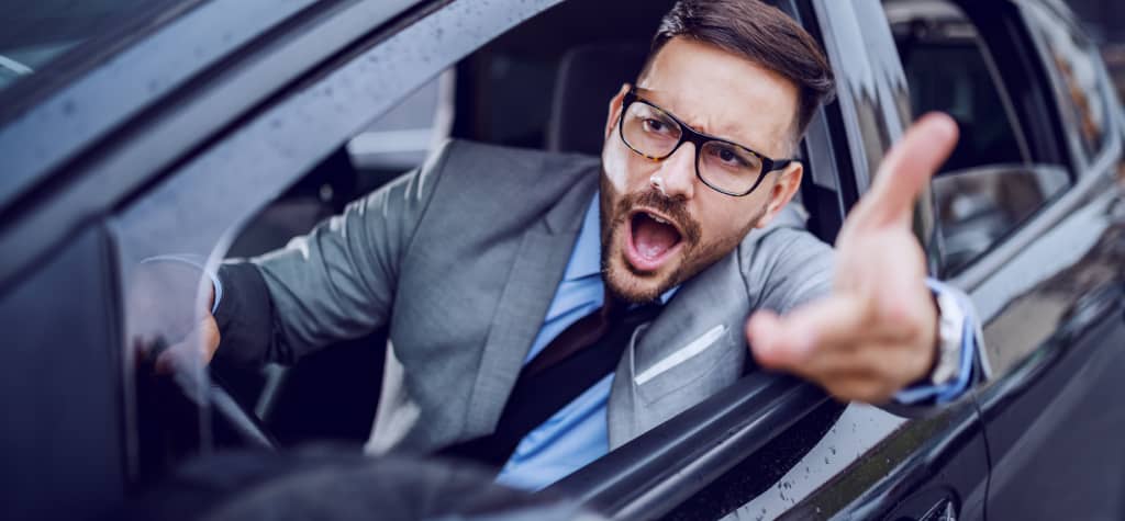 A businessman in a suit gestures from the open window of a black car, conveying urgency or excitement amidst a blurred background.